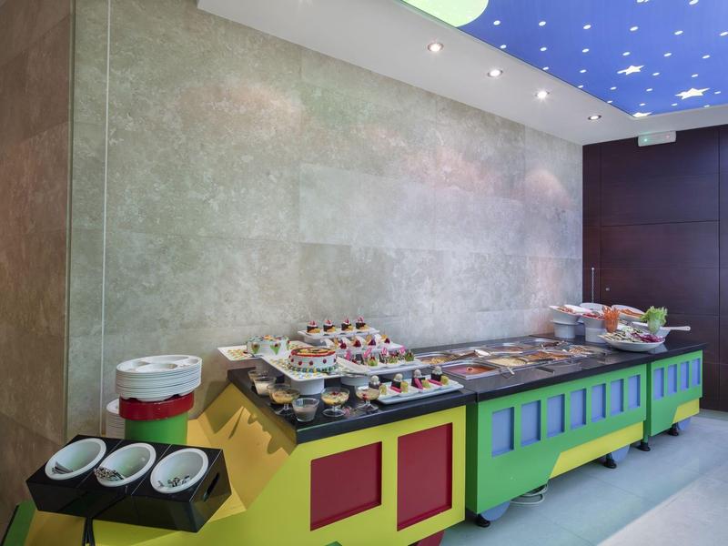 Kolorowy bufet z wypiekami i naczyniami w nowoczesnym wnętrzu hotelowym.