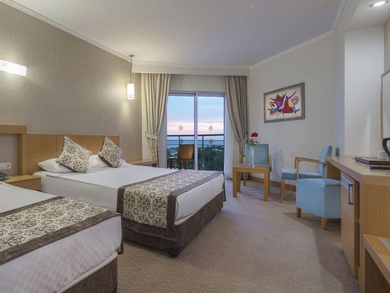 Pokój hotelowy z dwoma łóżkami, balkonem, telewizorem i prostym wystrojem.