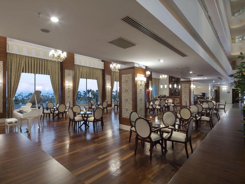 Elegancka przestrzeń hotelowa z drewnianą podłogą, okrągłymi stołami i krzesłami, dużymi oknami i żyrandolami.