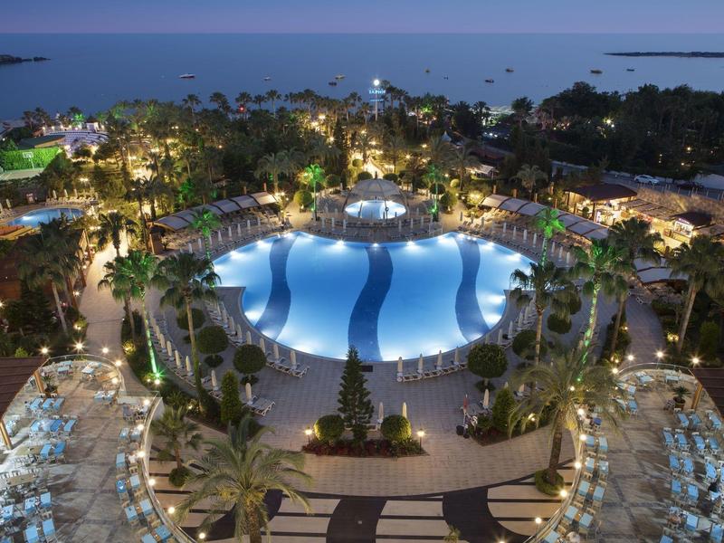 Widok nocny na okrągły basen w tropikalnym ośrodku nadmorskim z palmami i oświetleniem.