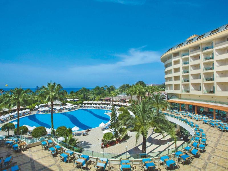 Hotel z basenem, leżakami i palmami pod czystym niebieskim niebem nad morzem.