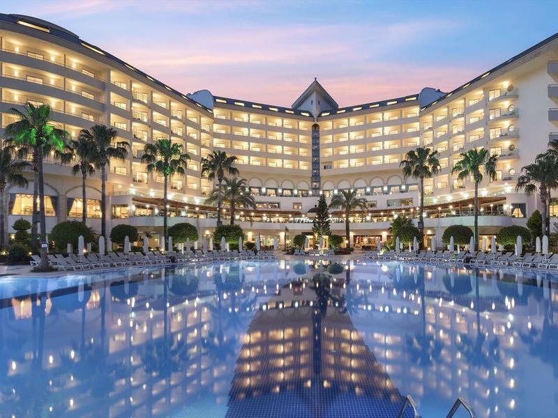 Luksusowy hotel z oświetlonym basenem i palmami o zachodzie słońca.