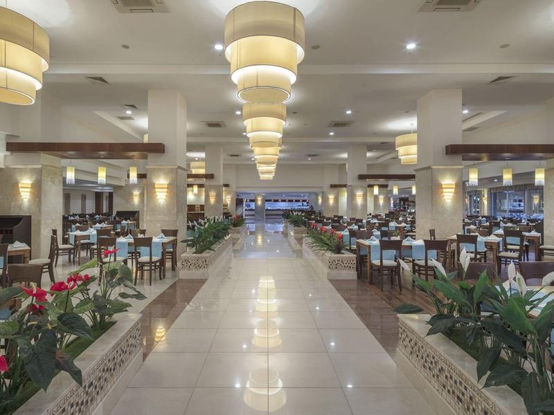 Duża, elegancka jadalnia z białymi stołami, wygodnymi krzesłami i jasnym oświetleniem