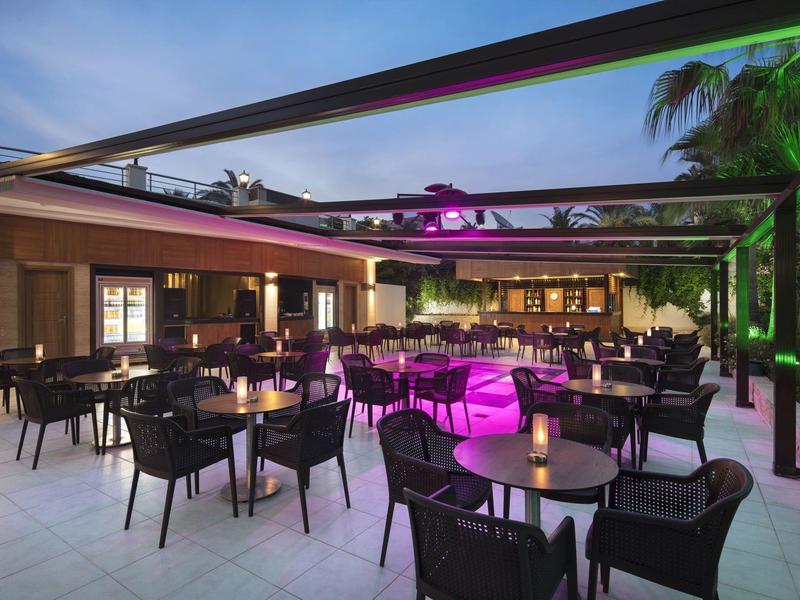 Zewnętrzny bar hotelowy z czarnymi stołami i krzesłami, oświetlony kolorowymi światłami.