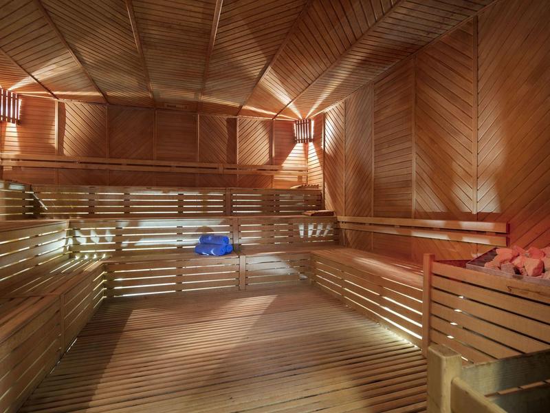 Wnętrze drewnianej sauny z wielopoziomowymi ławkami i przytłumionym oświetleniem.