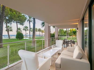 Balcone di un hotel con mobili bianchi e vista su un giardino con palme vicino al mare.