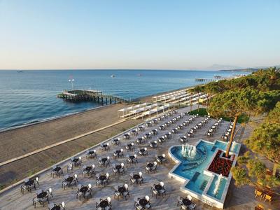 Strand mit Sonnenschirmen, Liegen, Pavillon und Pier am ruhigen blauen Meer bei klarem Himmel.