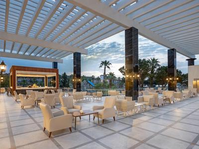 Große, offene Terrasse mit weißen Sesseln, Tischen und moderner Deckenstruktur bei Dämmerung.