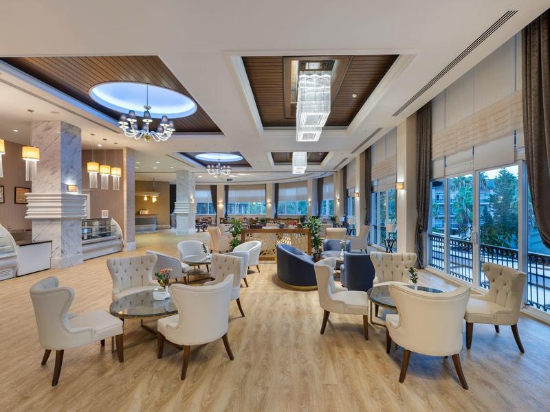 Großer heller Speisesaal mit runden Tischen, weißen Stühlen und großen Fenstern mit Blick ins Grüne.