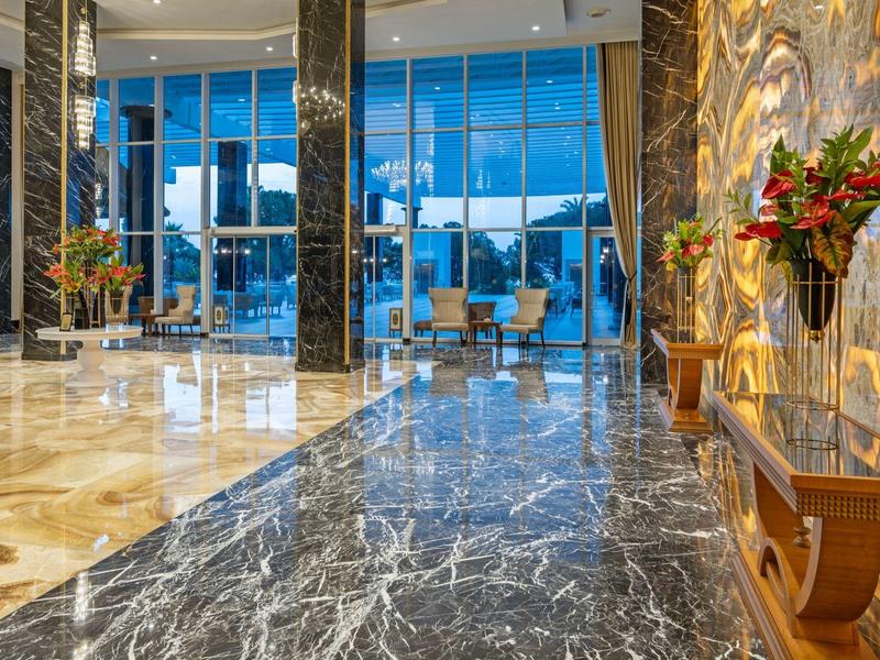 Große Hotellobby mit glänzendem Marmorboden, hohen Fenstern und Blumengestecken.