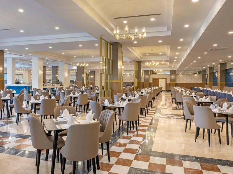 Großer heller Speisesaal mit vielen Tischen und beigen Stühlen, Marmorfliesen und moderner Beleuchtung.