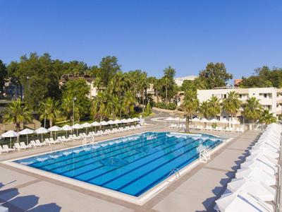 Large outdoor pool with sun loungers and umbrellas in a hotel complex on a sunny day.