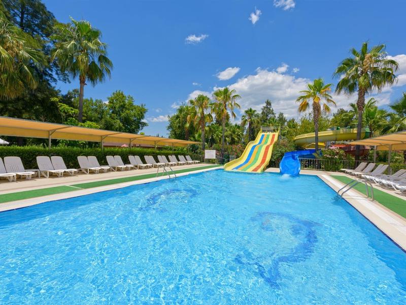Large outdoor pool with water slides, surrounded by lounge chairs and palm trees on a sunny day.