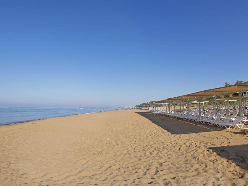 Wide sandy beach with sun loungers under clear blue sky