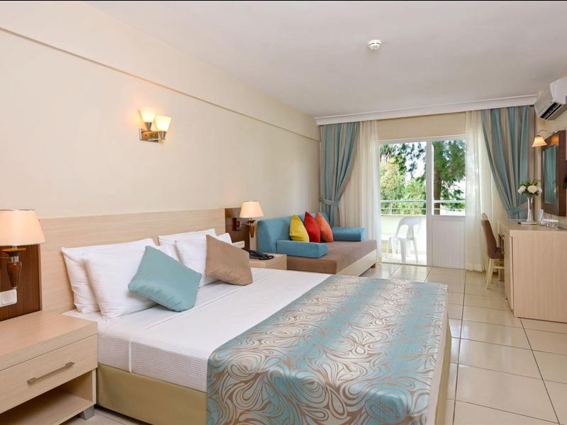 Bright hotel room with double bed, couch, balcony, and modern furniture.