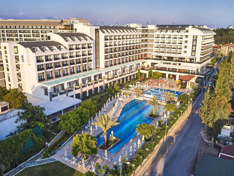 Velký vícepodlažní hotel se dvěma bazény, obklopený stromy.