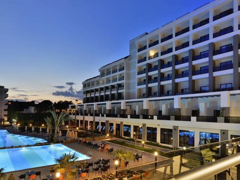 Hotel s osvětleným bazénem a terasou při západu slunce.