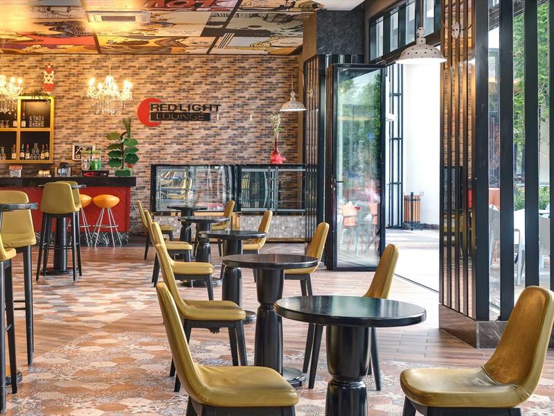 Moderní kavárna s kulatými stoly a žlutými židlemi u velkých oken a baru.