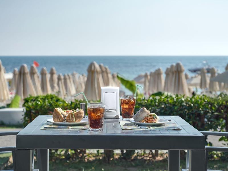 Stůl s nápoji a občerstvením na pláži s deštníky v pozadí.