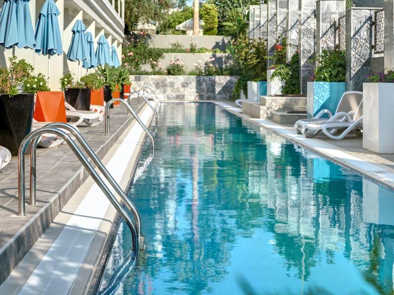 Moderní venkovní bazén s lehátky a modrými slunečníky na obou stranách.