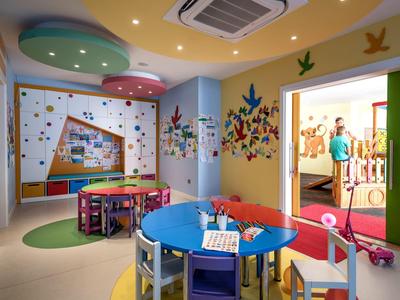 Sala de juegos colorida para niños con mesas, sillas y pared de escalada en un área de hotel.
