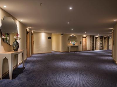 Amplio pasillo de hotel con alfombra, luces en el techo y decoraciones en las paredes.