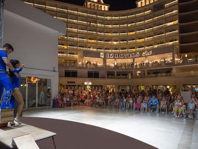 Dav sleduje představení na pódiu v polokruhovém osvětleném prostoru.