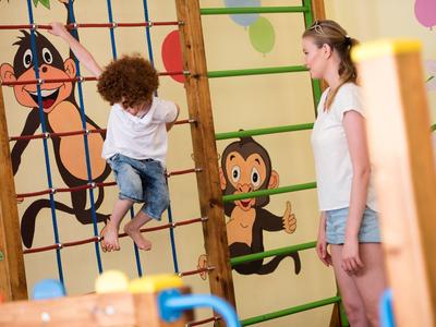Niño trepando una escalera de madera con dibujos de animales, mujer observa en habitación luminosa.