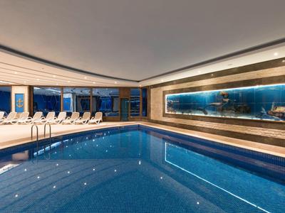 Piscina cubierta moderna con tumbonas y gran muro de vidrio en área de hotel lujoso.