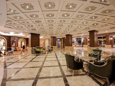 Gran vestíbulo de hotel con suelos de mármol elegantes, techo decorativo y áreas de descanso con sillones y mesas.