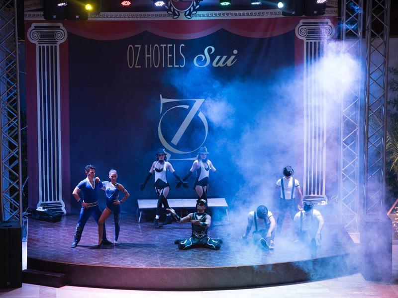 Escenario al aire libre con siete actores, iluminación azul y niebla.