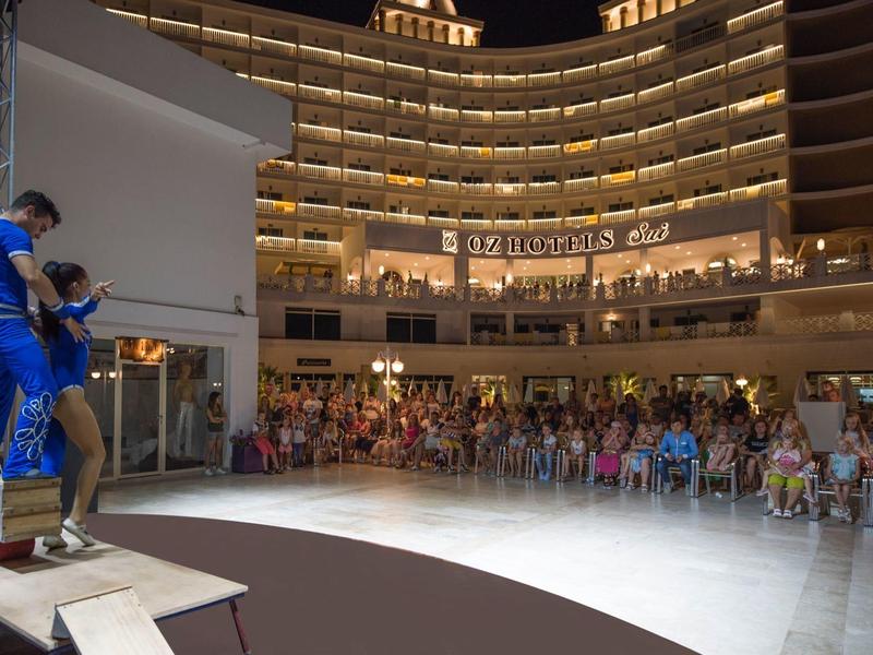 Personas sentadas frente a un balcón semicircular iluminado de hotel durante evento nocturno.