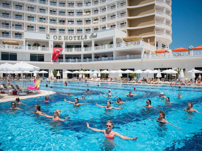 Un gran hotel con balcones curvos y una piscina llena de personas disfrutando del agua.