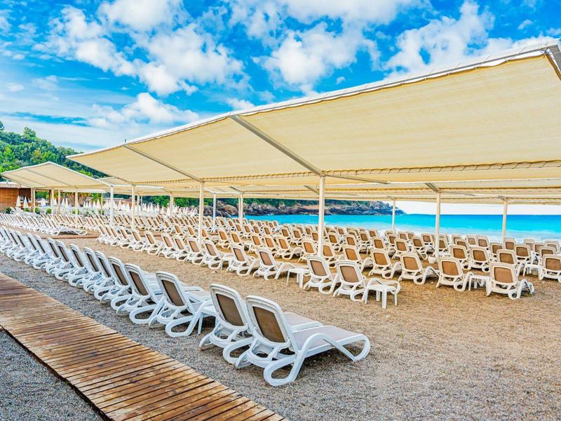 Muchas tumbonas blancas bajo grandes toldos en la playa con vista al mar azul.