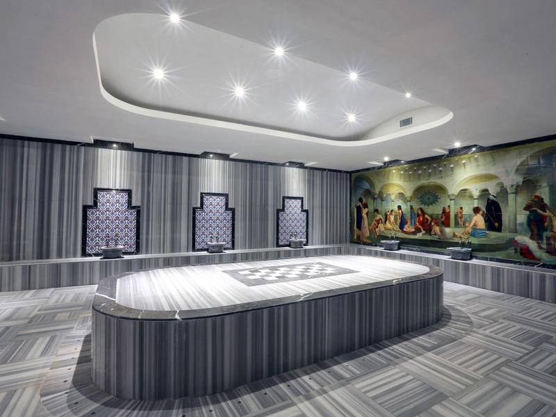 Hammam turco moderno con camas de mármol y un mural colorido en la pared.