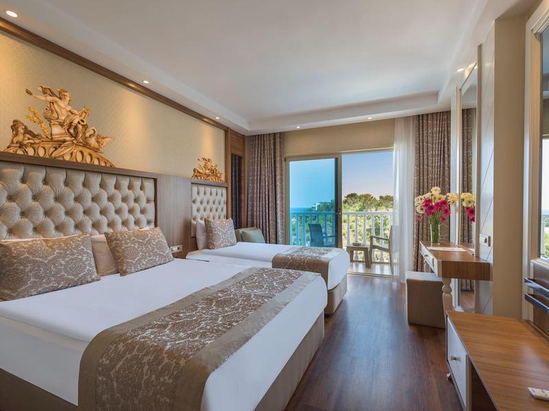 Habitación de hotel elegante con dos camas, vista al balcón y al mar, madera cálida y iluminación suave.