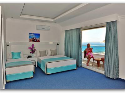 Hotel room with two beds, terrace, sea view, person sitting on balcony chair.