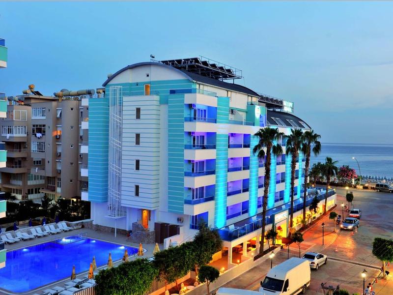 Modern hotel with pool, palm trees, and sea view at dusk.