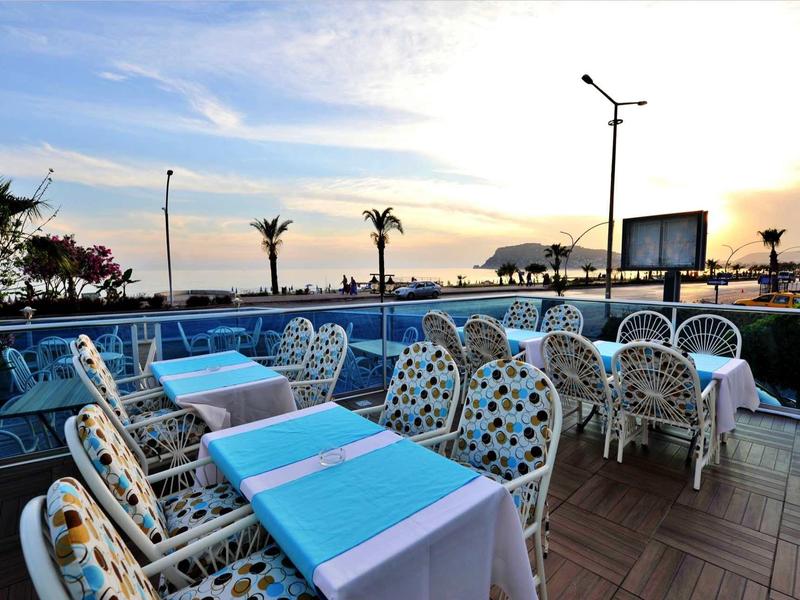 Outdoor restaurant area with tables, chairs, and a sunset view over the sea.