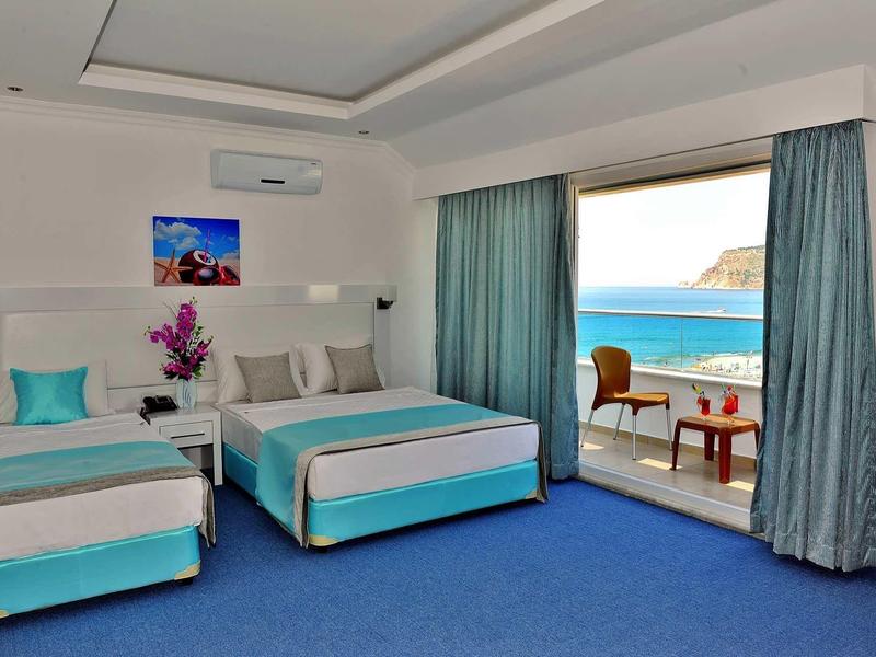 Hotel room with two beds, blue carpet, and balcony with sea view.