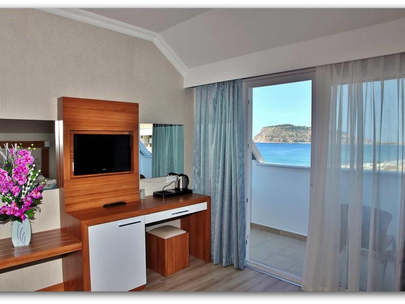 Hotel room with TV, minibar, vase with flowers, and sea view through balcony.