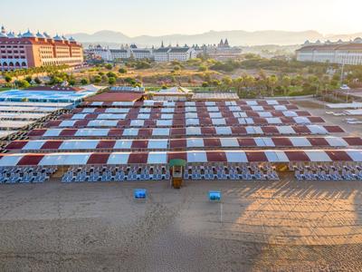 Strand mit Reihen von rot-weißen Sonnenschirmen und Liegestühlen bei Sonnenaufgang.