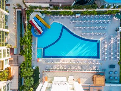 Großer rechteckiger Pool mit buntem Wasserrutschenbereich und vielen Liegestühlen in Reihen.