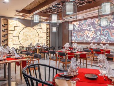 Elegantes Restaurant mit roten Tischen, schwarzem Mobiliar und dekorativen Wandlampen und Bildern.