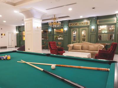 Sala giochi moderna con tavolo da biliardo verde, poltrone e decorazioni artistiche alle pareti.