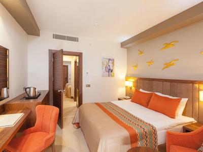 Hell eingerichtetes Hotelzimmer mit Doppelbett, orange Akzenten und modernem Mobiliar.