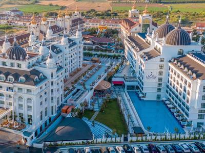 Großer Hotelkomplex mit weißen Gebäuden, Türmen, Pools und begrünten Innenhöfen bei Sonnenuntergang.