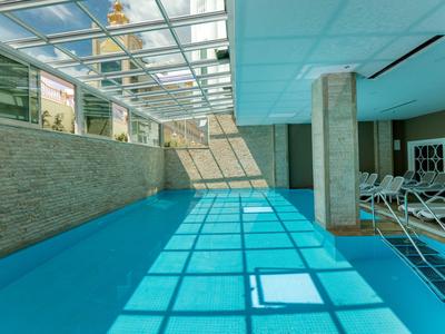 Area piscina interna con tetto in vetro, parete in pietra e lettini accanto alla piscina