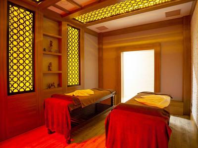 Zimmer mit zwei Massageliegen, rot-gelbe Beleuchtung und asiatisch inspiriertem Design.