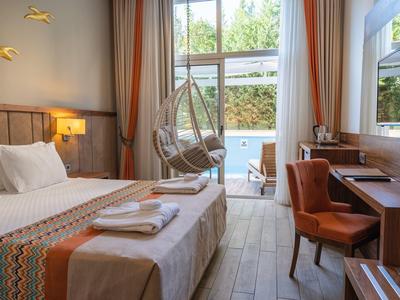 Hell eingerichtetes Hotelzimmer mit Doppelbett, Hängesessel, Schreibtisch und großer Fenstertür zum Garten.